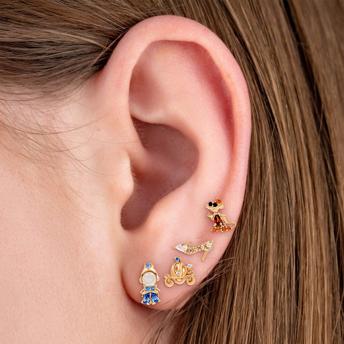 Close-up of an ear wearing gold Cinderella earring set with gemstones.
