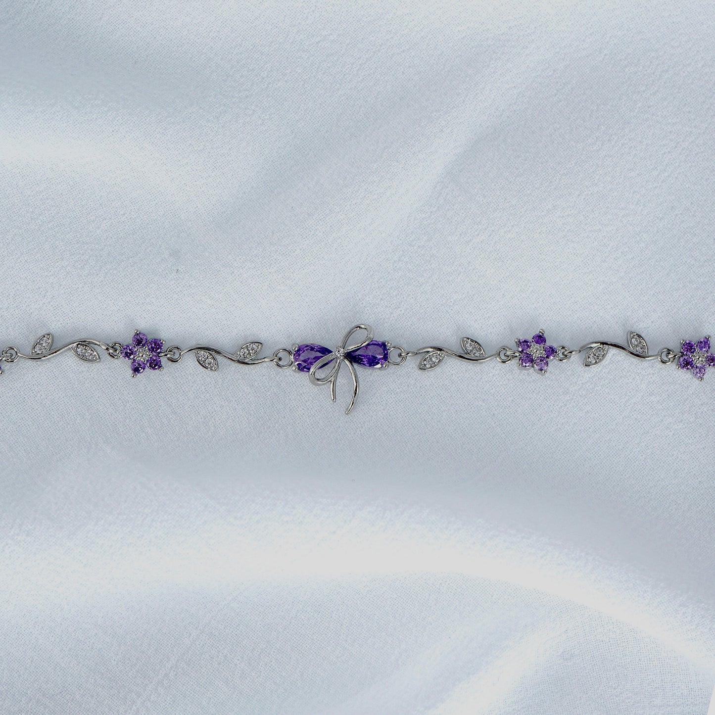 Silver bow bracelet with purple flowers on a white fabric background