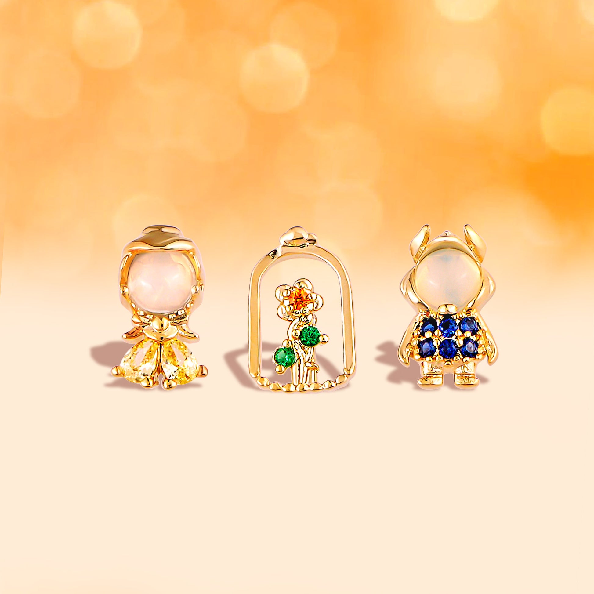 Three pairs of gold Beauty and the Beast earring with gemstones on a blurred orange background