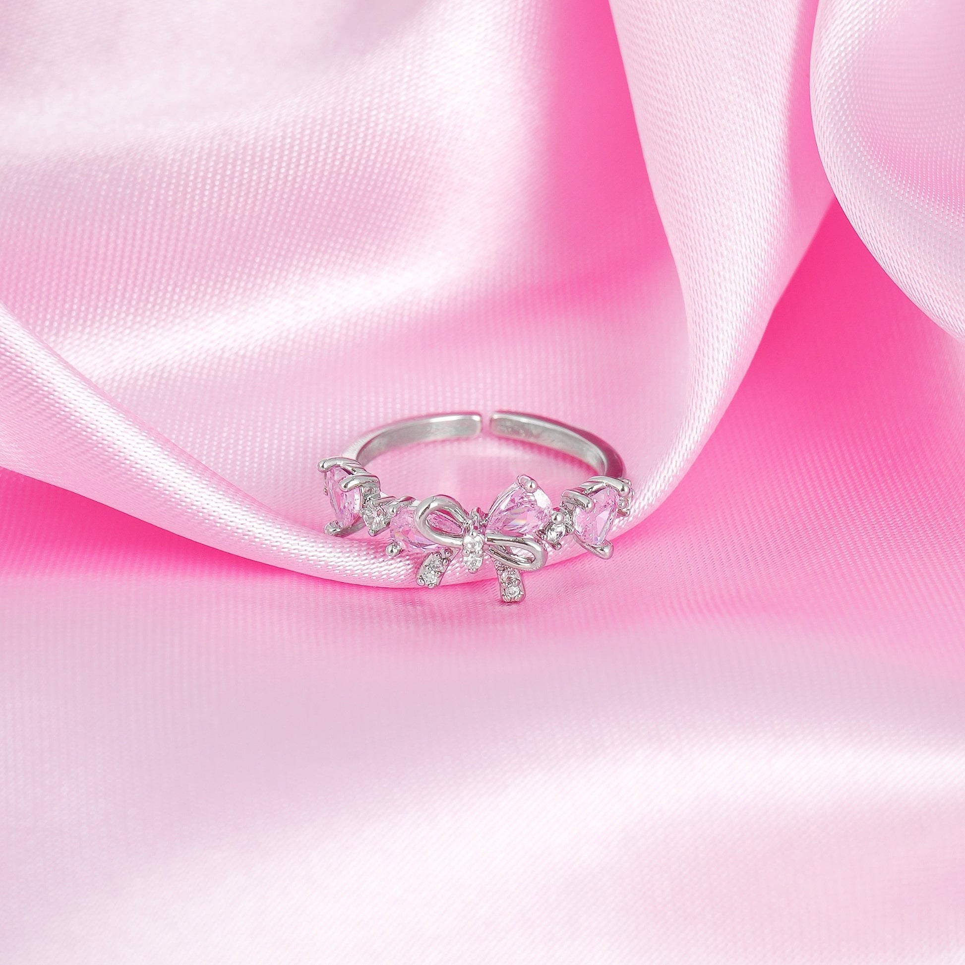 Silver ring with pink bow on a pink satin background