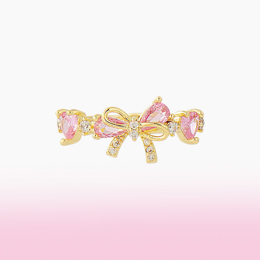Gold bow-shaped ring with pink bow on a gradient pink background