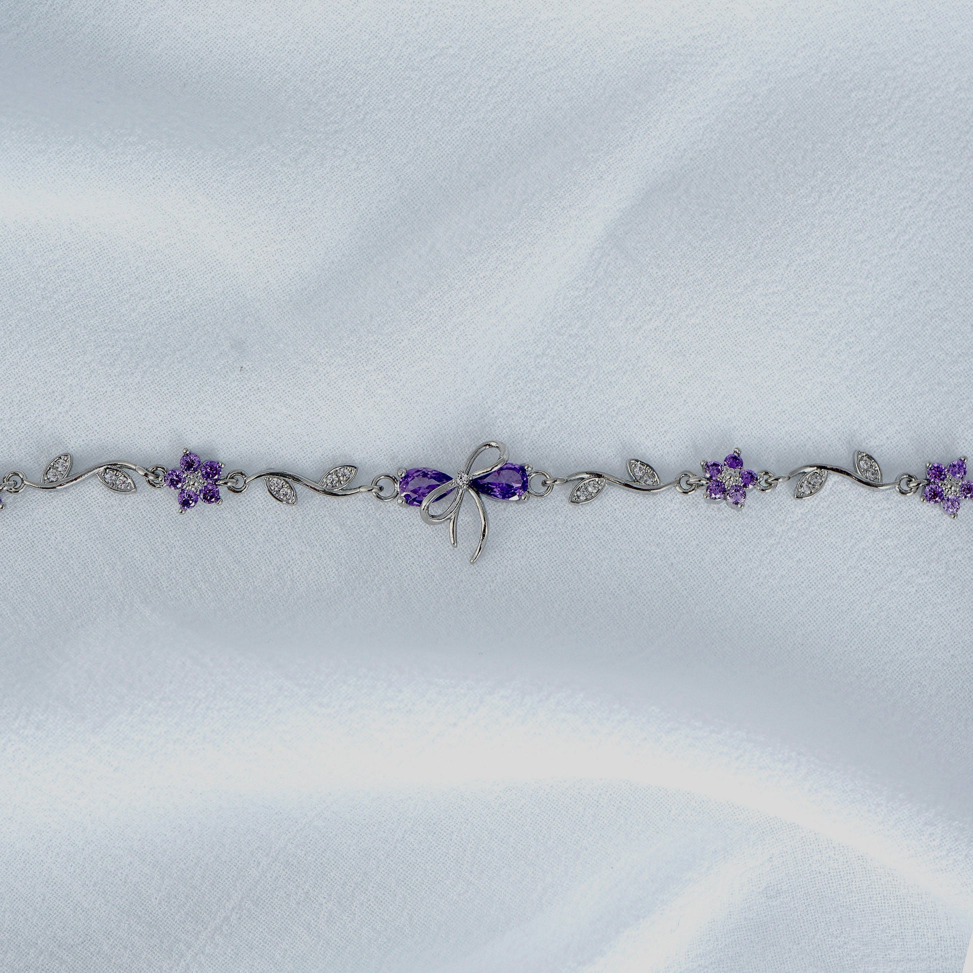 Silver bow bracelet with purple flowers on a white fabric background